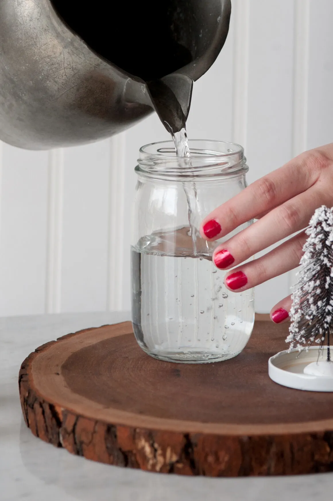 Female hands wearing red nail polish pouring water into a mason jar to make a snow globe