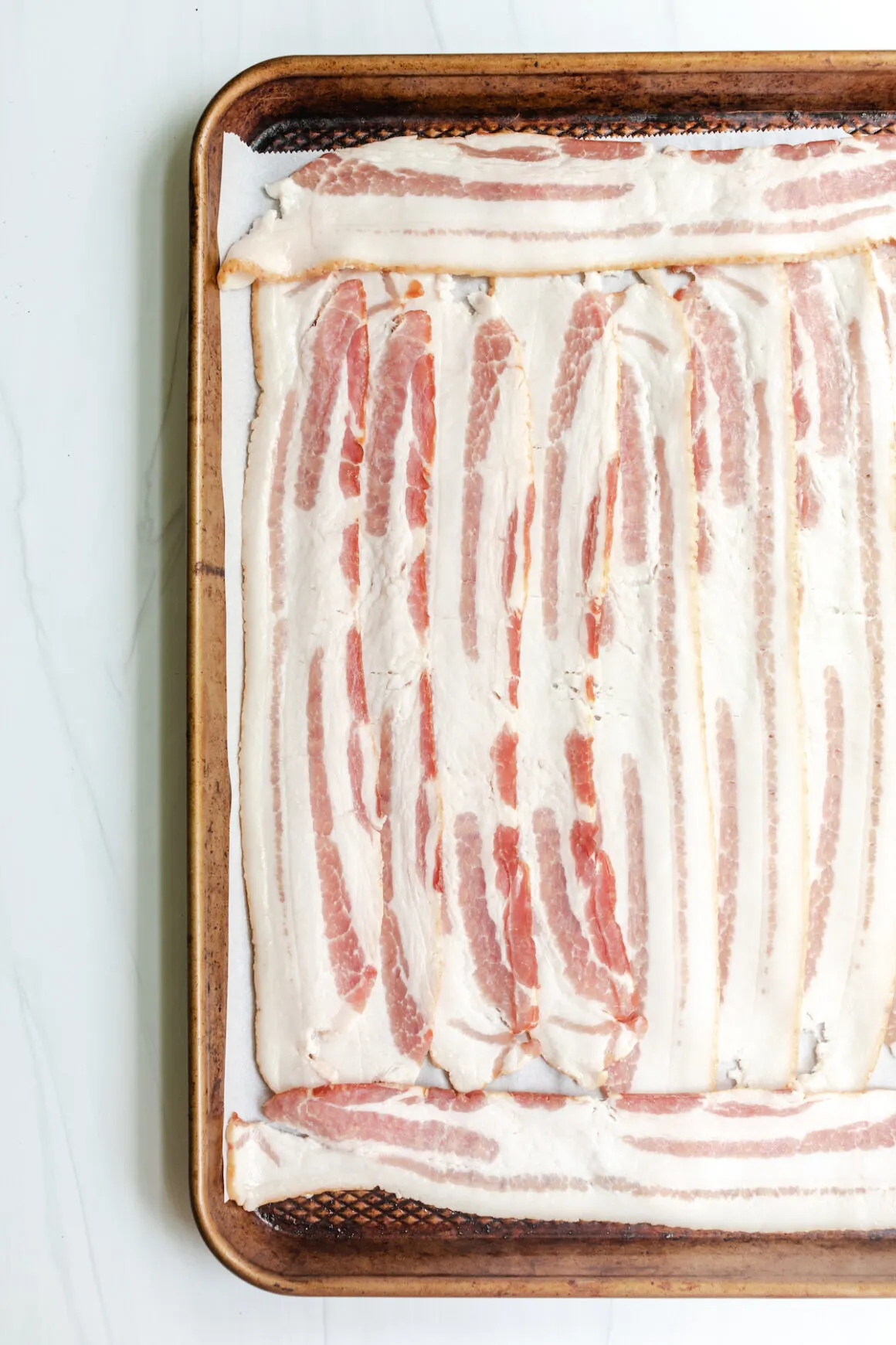 Thick cut bacon on a baking sheet with parchment paper