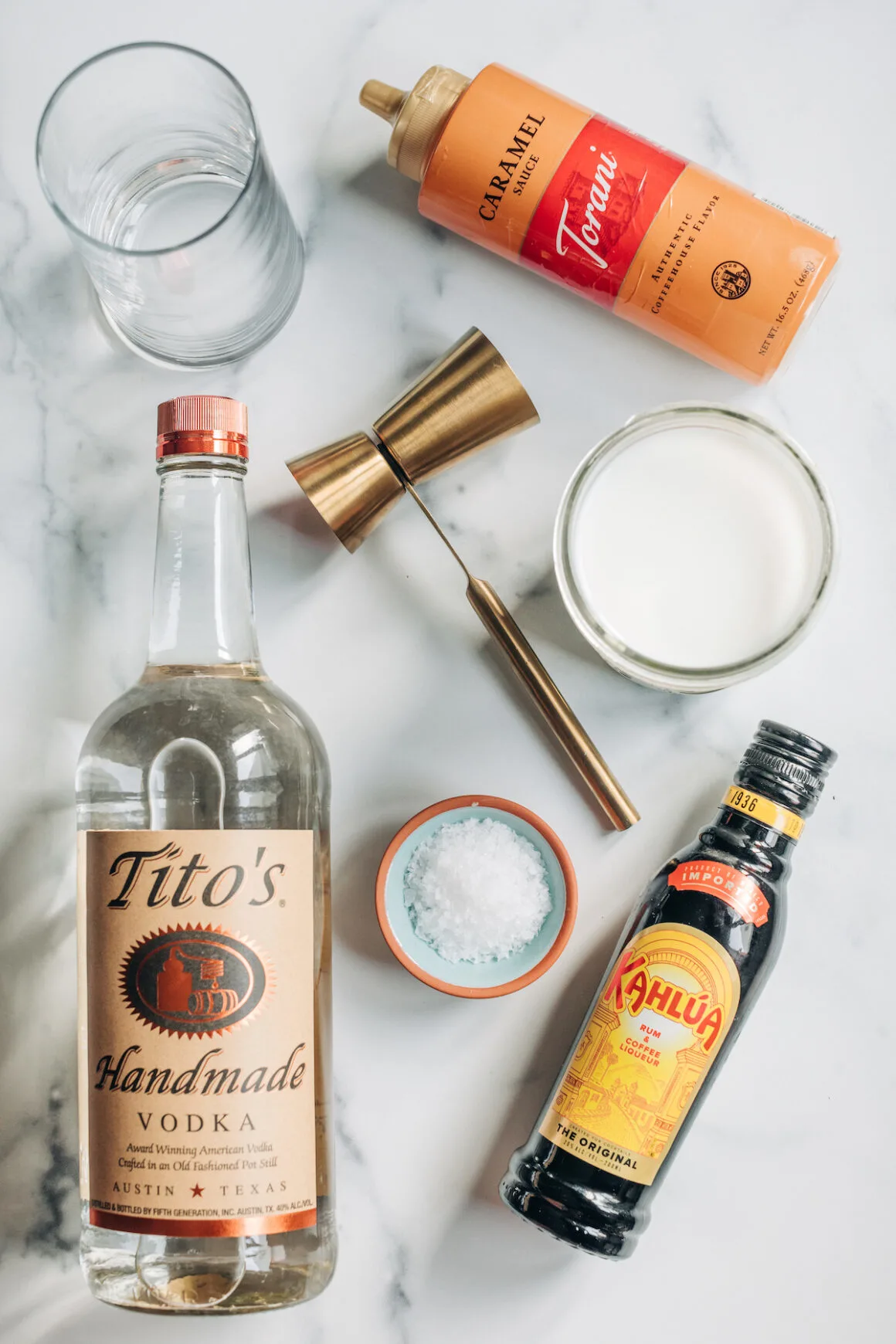 Ingredients to make a salted caramel White Russian cocktail including Tito's vodka and Kahlua