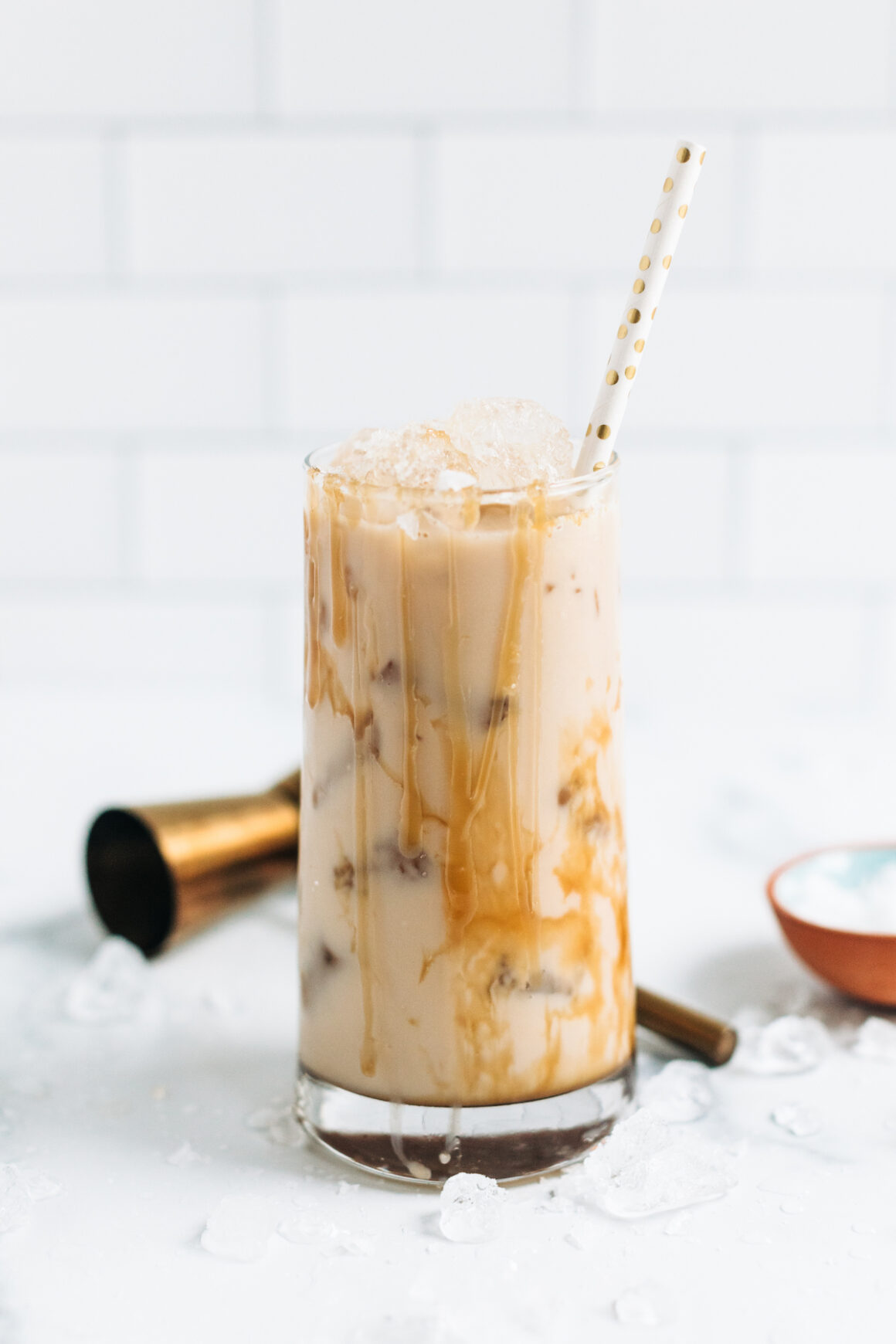 Tall rocks glass holding a White Russian cocktail drizzled with caramel sauce