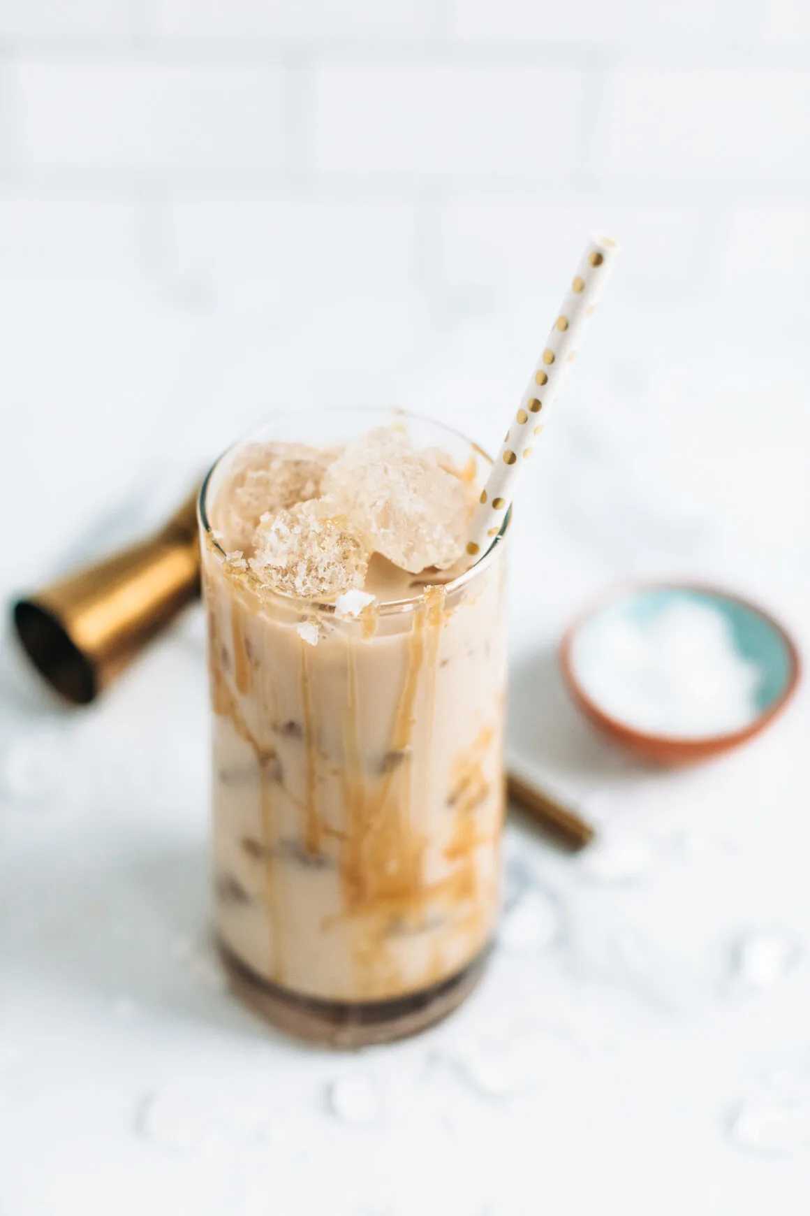 A salted caramel White Russian cocktail with a brass jigger and a paper straw