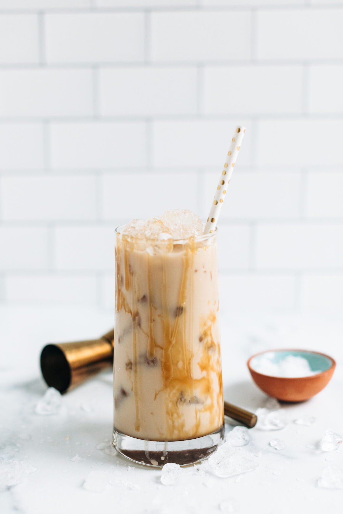 A salted caramel White Russian drink in a cocktail glass drizzled with caramel sauce with a paper straw