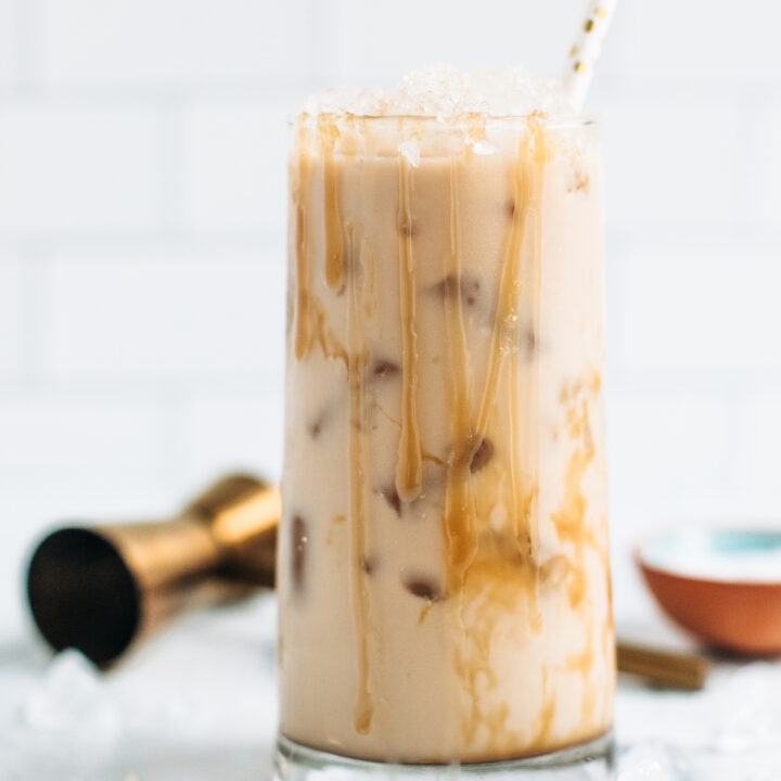 A salted caramel White Russian cocktail covered with drips of caramel sauce in a tall cocktail glass