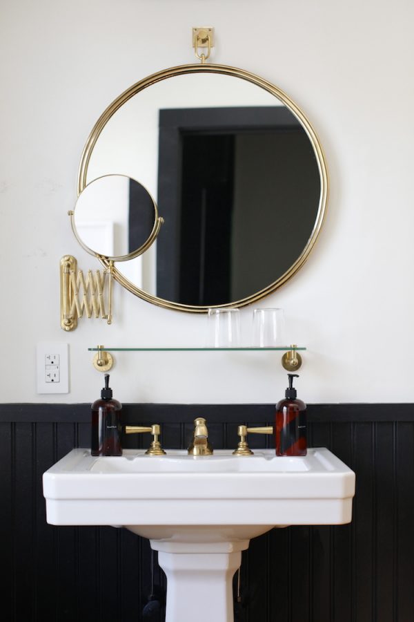 Black and brass bathroom with round mirror and pedestal sink