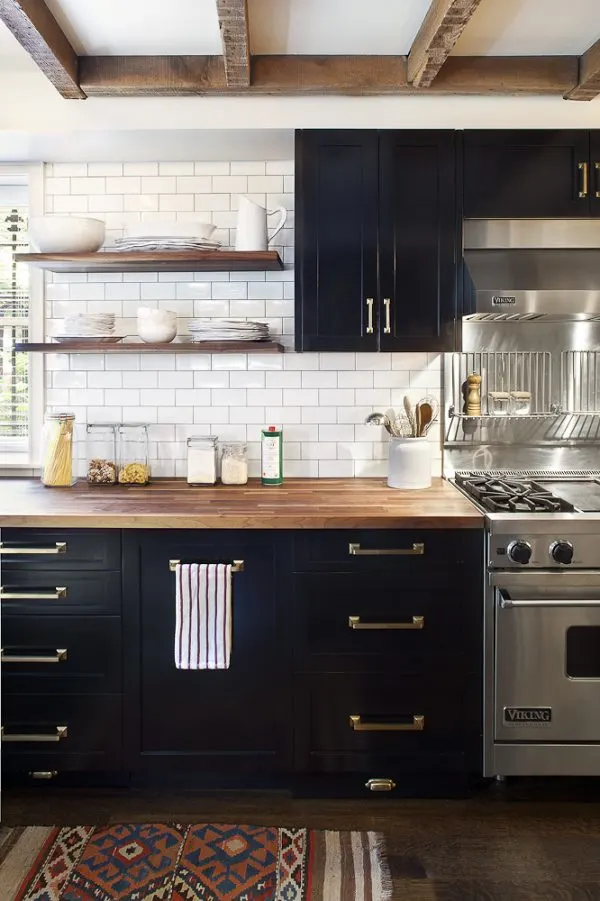 Kitchen with black cabinets, brass hardware, commercial range, subway tile backsplash, open shelving, butcherblock countertops